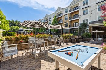 an outdoor patio with a pool table and umbrellas and an apartment building